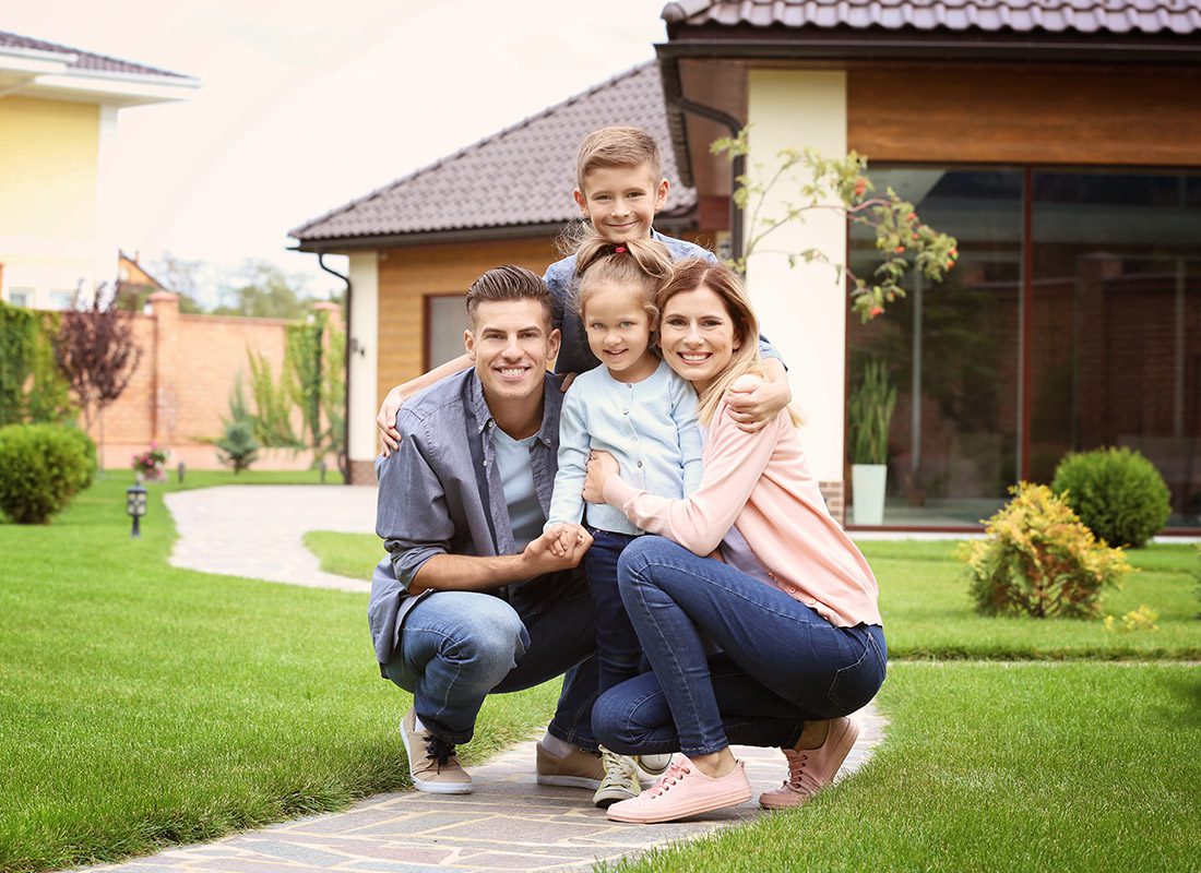 Personal Insurance - Happy Family Kneeling in Front of Their Home on a Sunny Day